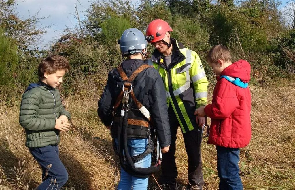 Un adulte attache des sangles sur un enfant pour une visite sur chantier.